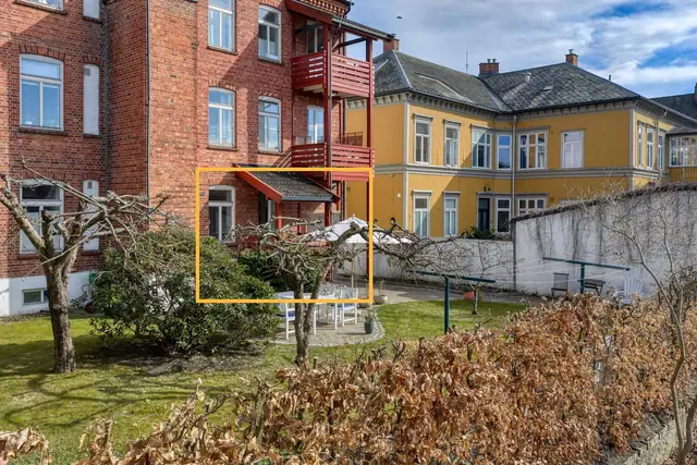 Beliggende i første etasje med balkong og vinduer ut mot en stor, fin hage der kveldssolen slipper inn.