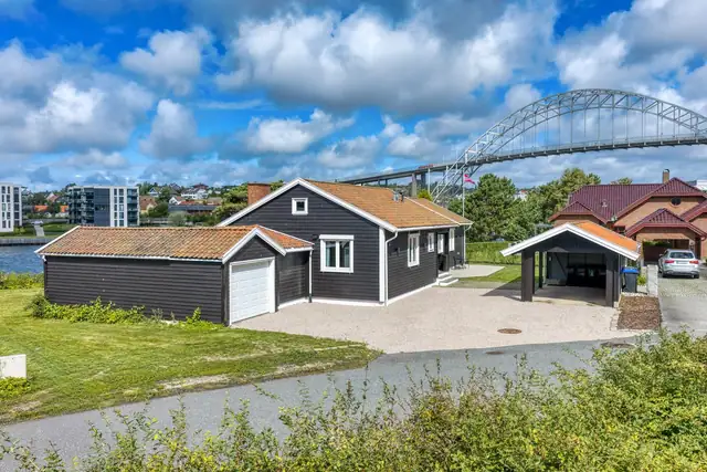 Fra gaten, med garasje, stor gårdsplass og carport.  I bakgrunnen den ikoniske Fredrikstadbroa.